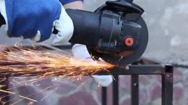 Close-up of an angle grinder cutting rebar. Female hands in work gloves holding a cordless grinder and cutting rebar into small pieces. Power tool for construction and repair work