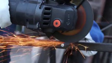 Close-up of an angle grinder cutting rebar. Female hands in work gloves holding a cordless grinder and cutting rebar into small pieces. Power tool for construction and repair work