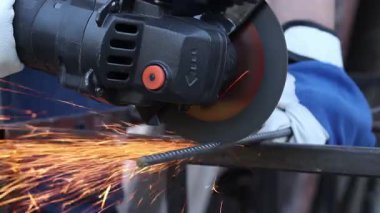 Close-up of an angle grinder cutting rebar. Female hands in work gloves holding a cordless grinder and cutting rebar into small pieces. Power tool for construction and repair work