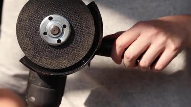 Close-up of female hands holding a cordless grinder. Woman screws a handle to a cordless grinder. Power tool for construction and repair work. Close-up of an angle grinder. Grinder with a metal disc