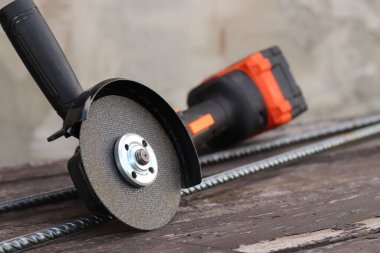 Kablosuz öğütücü, takviyenin yanındaki ahşap yüzeyde, yakın plan. Kulübede ya da şantiyede onarım. Kablosuz kablosuz öğütücü. Elektrikli alet. DIY tamir konsepti