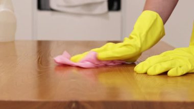 Cleaning lady wipes kitchen table. Woman in apron and yellow gloves wipes table with viscose napkin. Cleaning apartment from dust and dirt. Cleaning service. Close-up of hands in cleaning gloves