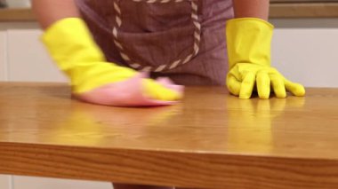 Cleaning lady wipes kitchen table. Woman in apron and yellow gloves wipes table with viscose napkin. Cleaning apartment from dust and dirt. Cleaning service. Close-up of hands in cleaning gloves
