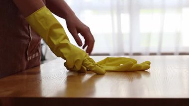 Cleaning lady wipes kitchen table. Woman in apron and yellow gloves wipes table with viscose napkin. Cleaning apartment from dust and dirt. Cleaning service. Close-up of hands in cleaning gloves