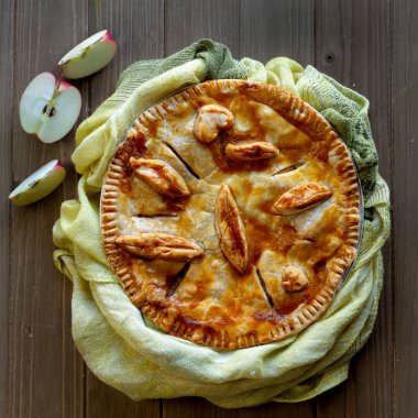 Elmalı pasta hamur yapraklarda yeşil bulaşık bezi ile dekore edilmiş ve üstten Bakınlan ahşap masa üzerinde yarıya elma kesme-hasat gıda kavramı