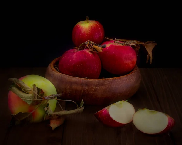 Bowl with  assorted apples against black background with one whole and one cut apple on wooden table- fall composition