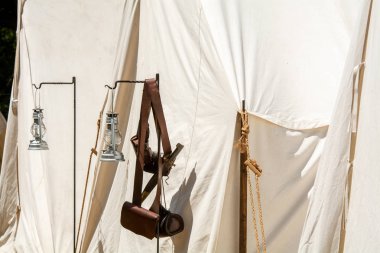 Deri kartuş kutuları, bir iç savaş kampı düşündüren bir tuval çadır dışında asılı bıçak ve gaz lambaları