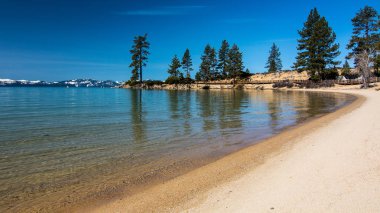 Lake Tahoe North, Nevada ilçe, Kaliforniya, ABD, mavi şeffaf su, kumlu kıyı ve birkaç bulutlar ile mavi bir gökyüzü gün arka plan dağları ve çam ağaçlarının tepesinde kar featuring Sand Harbor plaj Uzun pozlama
