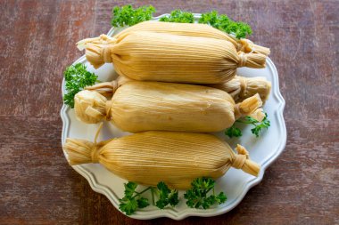 Unwrapped yığılmış Meksika tamales grunge ahşap masada yeşil maydanoz yaprakları ile süslenmiş beyaz plaka, yukarıdan bakıldığında - etnik Gıda kavramı