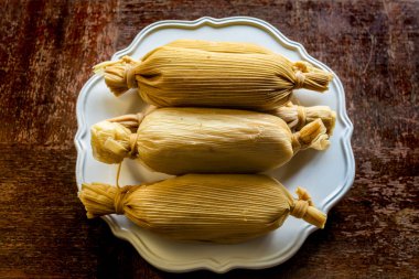 Yukarıdan görüntülenen grunge ahşap masa üzerinde beyaz plaka üzerinde unwrapped yığılmış Meksika tamales - etnik Gıda kavramı