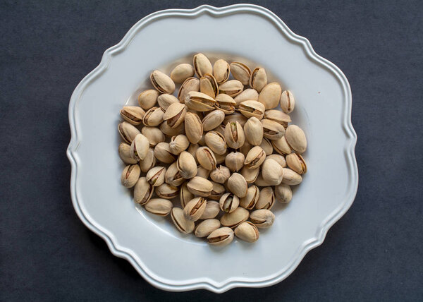  Raw pistachios in white plate close-up against black background- healthy food concept