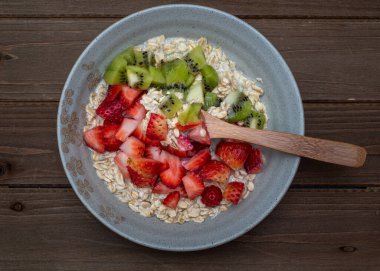 Tahta masada doğranmış çilek ve kivi ile dekore edilmiş yulaf ezmesi, tabağın tamamı, merkezde, üst manzara, çatal kaşıkla.