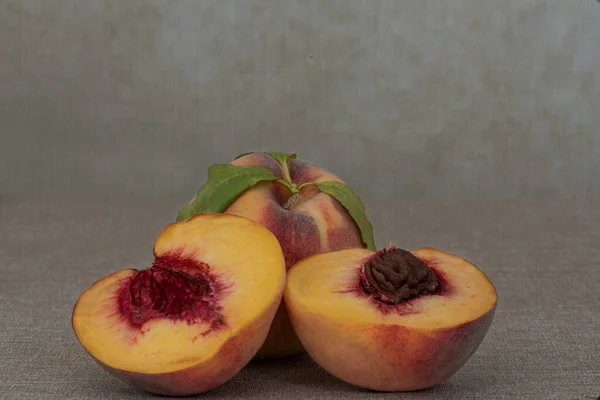 Two fresh yellow peaches on brown table, one whole and one cut in half, centered, with macro detail , side view- harvest still life, with plenty of copy-space