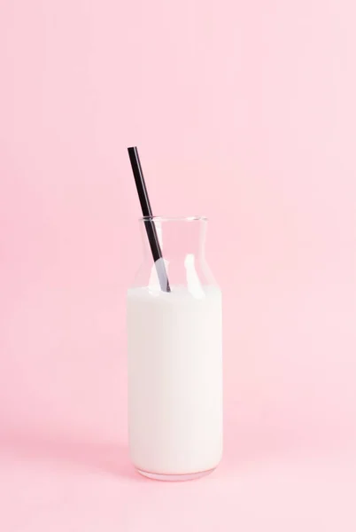 Şık şişeyi pastel pembe bir arka plan üzerinde. Siyah şişeyi saman. Minimalist bir kahvaltı kavramı.