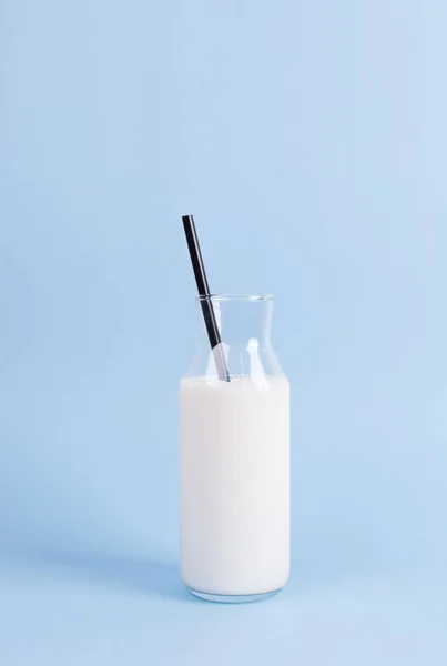 在柔和的蓝色背景上的时尚牛奶瓶 瓶子里有黑稻草 简约早餐的概念 — 图库照片