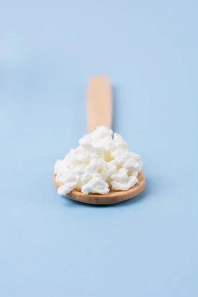 Taze ev yapımı peynir bir tahta kaşık yakın çekim pastel mavi bir arka plan üzerinde. Minimalizm. Sağlıklı beslenme kavramı.