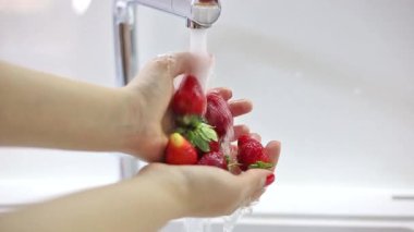 Kadın el ele tutuşup taze çilek yıkıyor. 