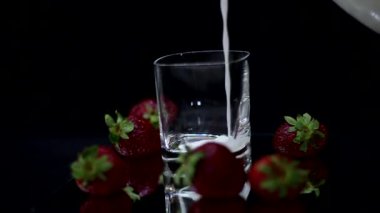 siyah arka planda taze kırmızı çilek ile cam içine süt koyarak  