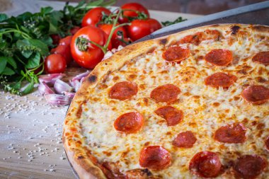 Pepperoni pizza ve yemek malzemeleri: domates, fesleğen, ahşap masa zemininde sarımsak.