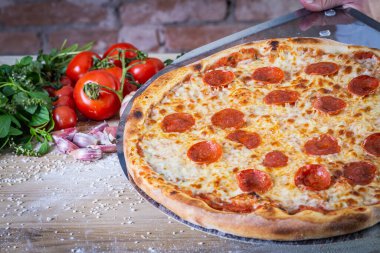 Pepperoni pizza ve yemek malzemeleri: domates, fesleğen, ahşap masa zemininde sarımsak.
