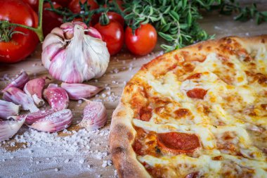 Pepperoni pizza ve yemek malzemeleri: domates, fesleğen, ahşap masa zemininde sarımsak.
