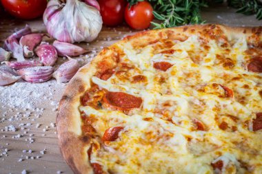 Pepperoni pizza ve yemek malzemeleri: domates, fesleğen, ahşap masa zemininde sarımsak.
