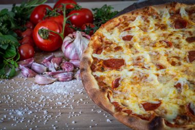 Pepperoni pizza ve yemek malzemeleri: domates, fesleğen, ahşap masa zemininde sarımsak.