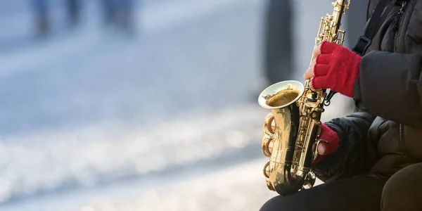person in red gloves Playing music on saxophone in street, winter season