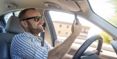 gülümseyen mutlu beyaz adam cep telefonu üzerinde sürüş araba ve alma selfie güneş gözlüğü 