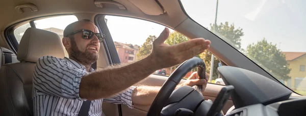 aggressive displeased man in sunglasses driving car and gesturing with hand