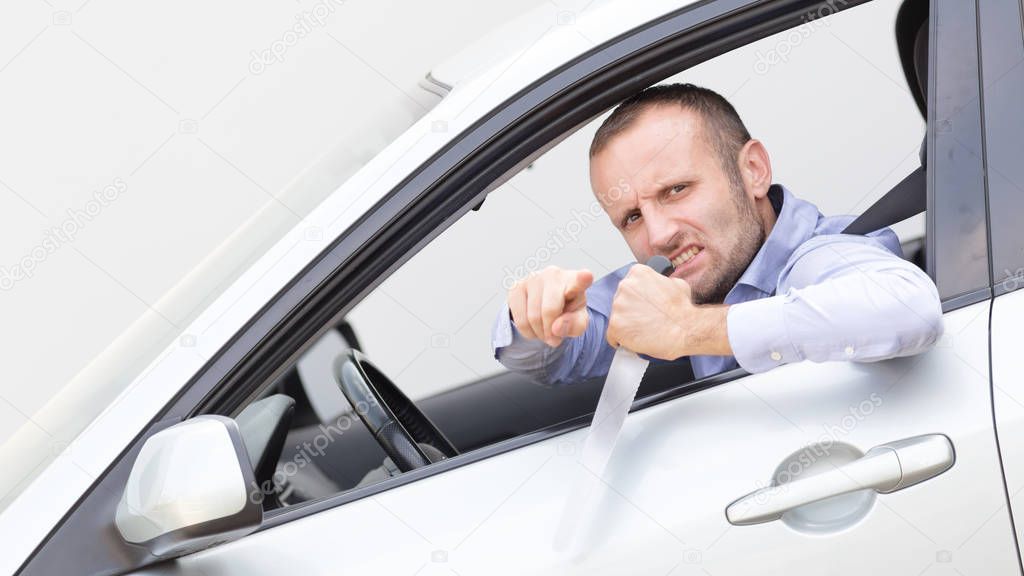 Aggressive and violent driver armed with a big kitchen knife. Copy space on the gray background.