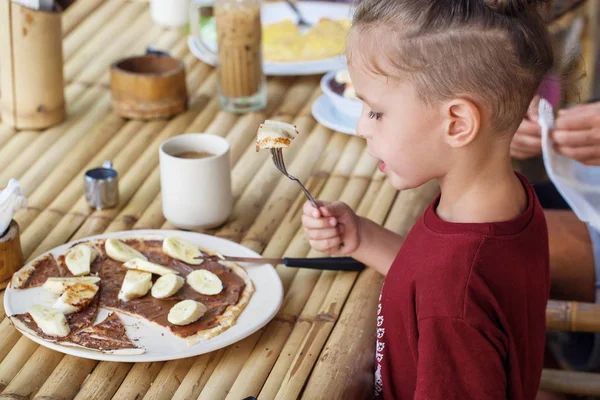 Boy eating pancake with banana and chocolate — Stock Photo, Image