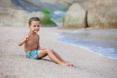 Çocuk kum deniz kenarında oturup...