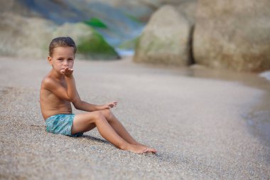 Çocuk kum deniz kenarında oturup...