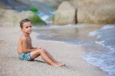 Çocuk kum deniz kenarında oturup...