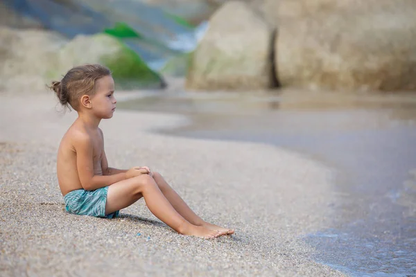 Jongen zit op het zand bij de zee — Stockfoto