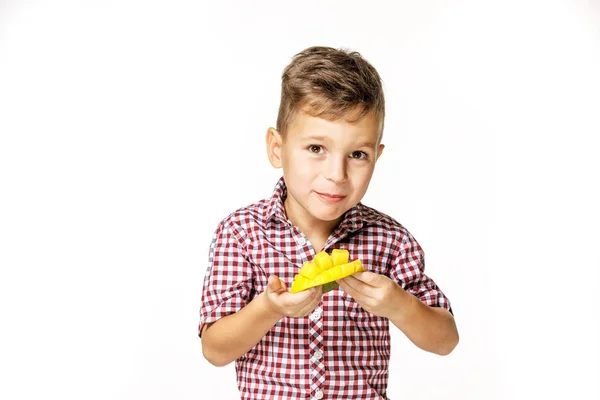 Красивый мальчик в красной рубашке ест манго — стоковое фото