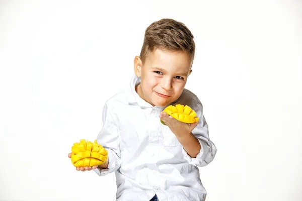 Snygg pojke i en vit skjorta äter en mango — Stockfoto