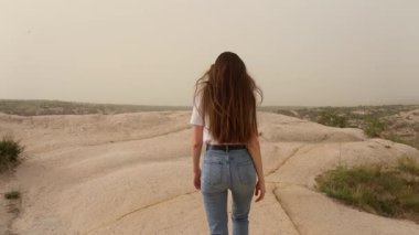 Türkiye 'nin başkenti Cappadocia' da kayalık bir tepede yürüyen tanınmayan esmer kadın çöl manzarasının, kum fırtınasının, özgürlüğü kucaklayan, gezgin şehvetin tadını çıkarıyor. Tur rehberi. Arkadan bak. Kamera takip etsin. İzleme görüntüsü