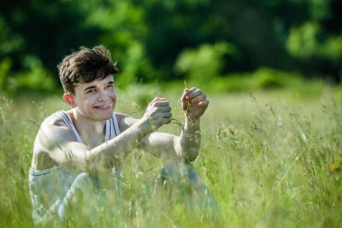 Uzun otların arasında sıcak bir yaz gününde oturan genç yetişkin erkek