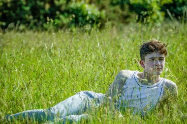 Sıcak bir yaz gününde amoung uzun çim döşeme genç bir yetişkin erkek