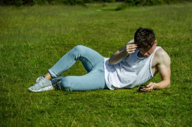 Dışarıda çimenlerin üzerinde sıcak bir yaz gününde ise döşeme bir cep telefonu kullanarak bir yonug yetişkin erkek