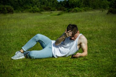 Dışarıda çimenlerin üzerinde sıcak bir yaz gününde ise döşeme bir cep telefonu kullanarak bir yonug yetişkin erkek