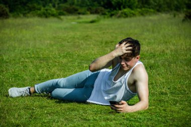 Dışarıda çimenlerin üzerinde sıcak bir yaz gününde ise döşeme bir cep telefonu kullanarak bir yonug yetişkin erkek