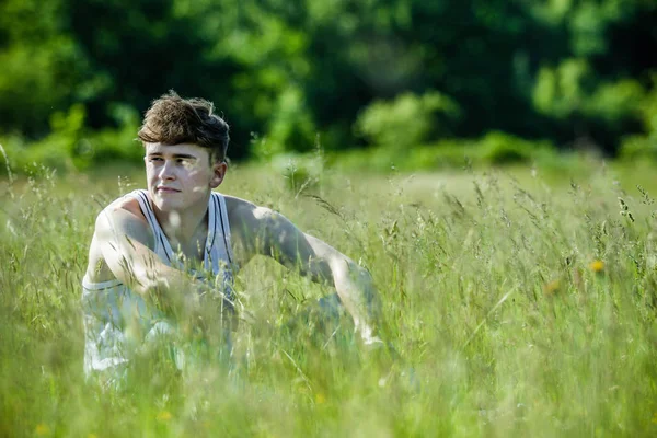 Uzun otların arasında sıcak bir yaz gününde oturan genç yetişkin erkek