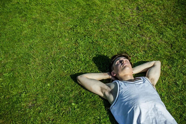 A young adult male sunbathing, laying on short grass on a warm summer\'s day