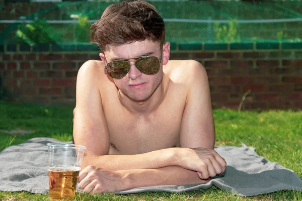 Young male adult laying in the sun with a beer