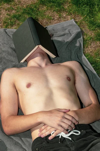 年轻男性成人躺在阳光下睡在书下 — 图库照片