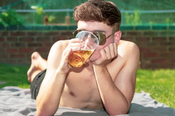 Young male adult laying in the sun with a beer