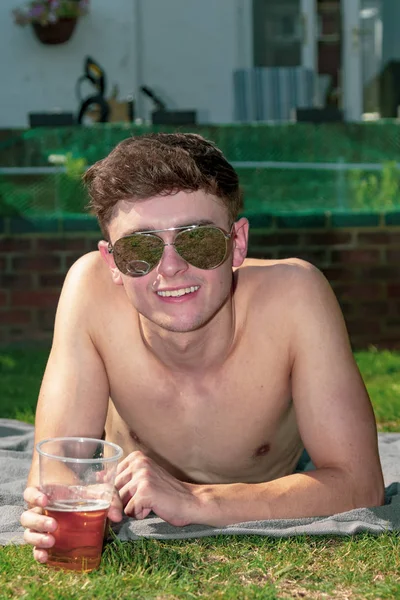 Young male adult laying in the sun with a beer